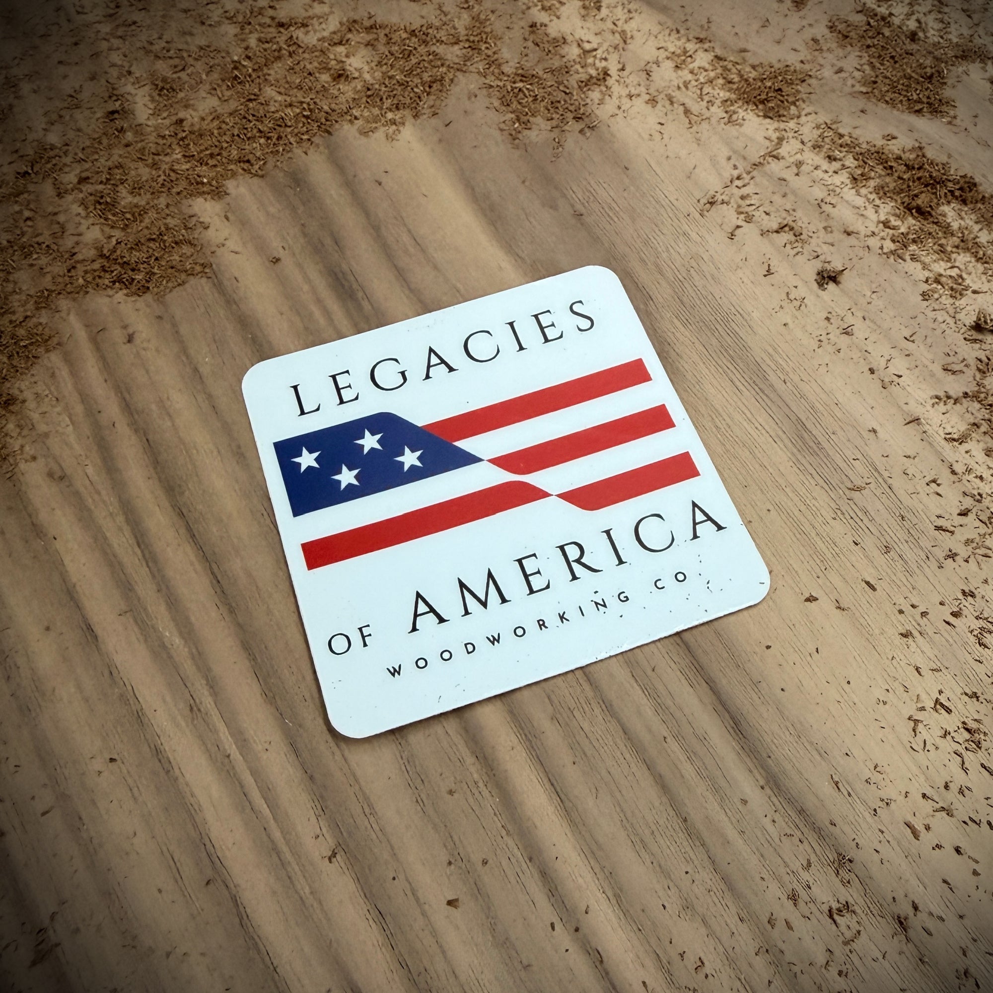 Legacies of America Woodworking Co. 3 inch logo sticker laying on a Walnut board in sawdust