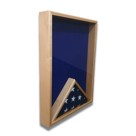Steep left angle view of a maple 18x24 vertical shadow box showing the depth of the case, with blue felt backing and a folded American flag inside