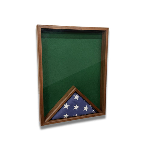 Walnut 18x24 vertical shadow box shown at a slight left angle with green felt backing and a folded American flag inside