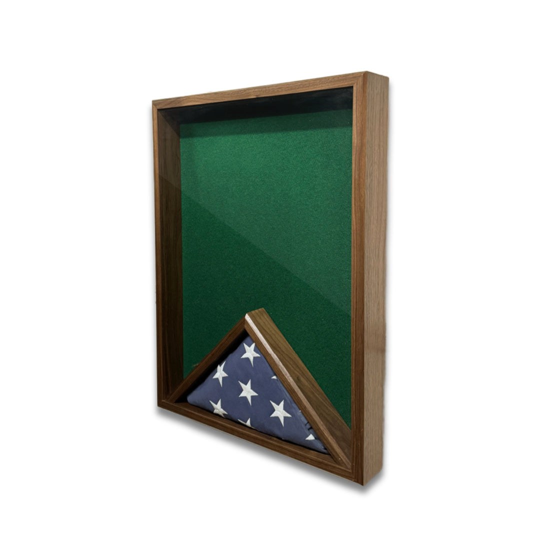 Walnut 18x24 vertical shadow box shown at a slight right angle with green felt interior and a folded American flag inside